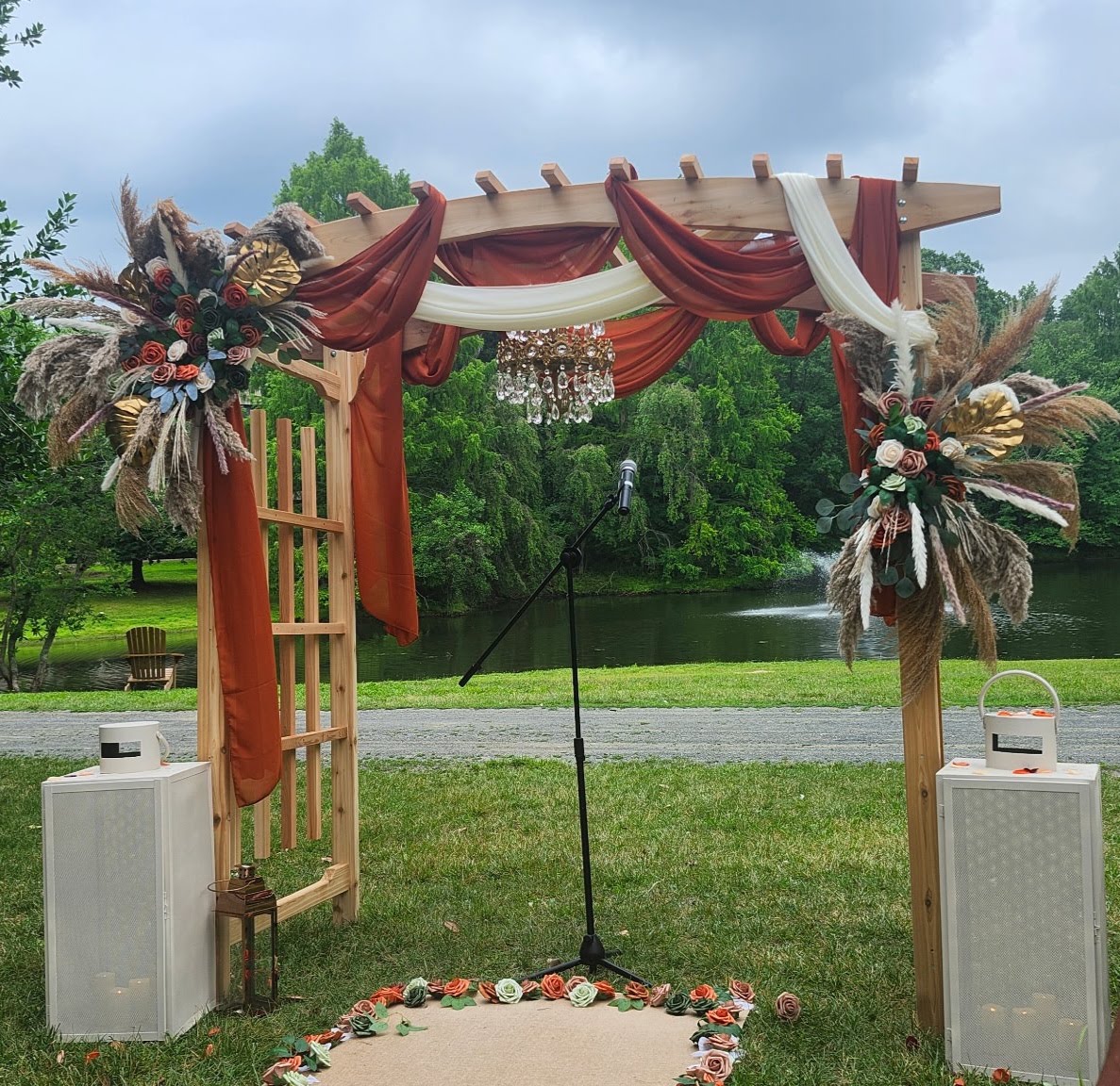 Wooden wedding pergola with rust and ivory drapery, crystal chandelier, roses and pampas grass